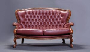 Elegant leather Chesterfield sofa with buttoned upholstery and carved wooden legs, set against a grey background.
