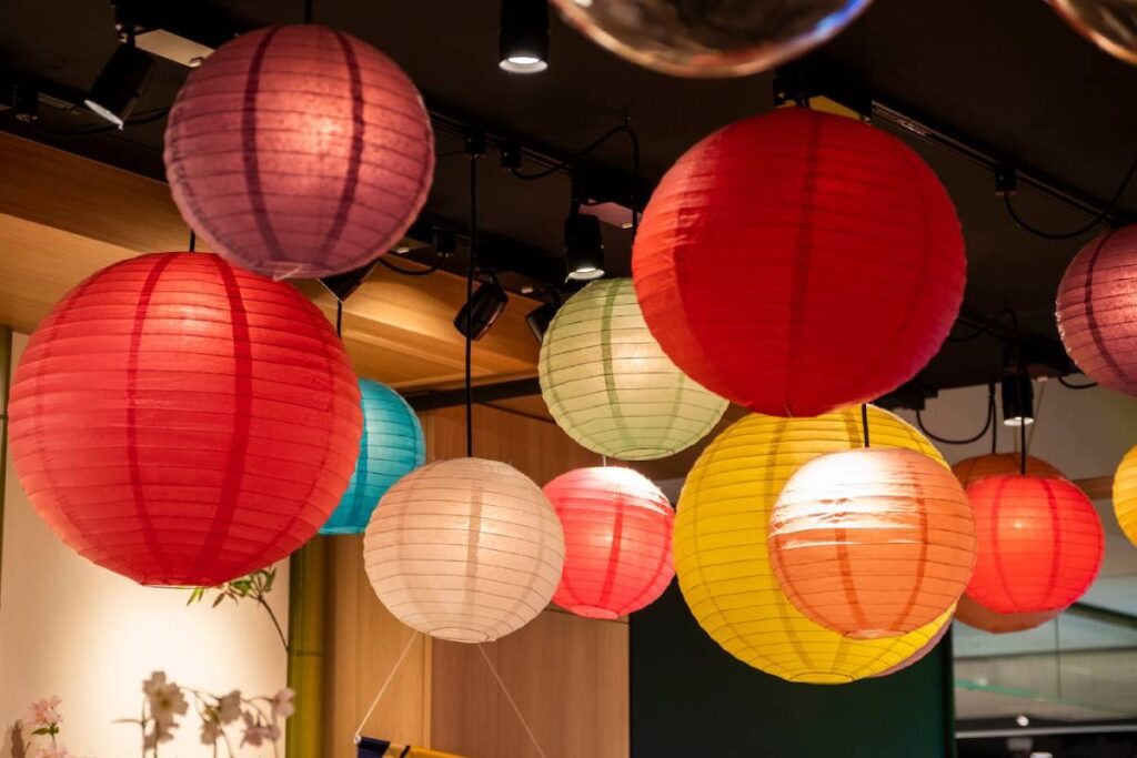Colourful paper lanterns hanging from a ceiling, creating a warm, festive atmosphere in an interior space.