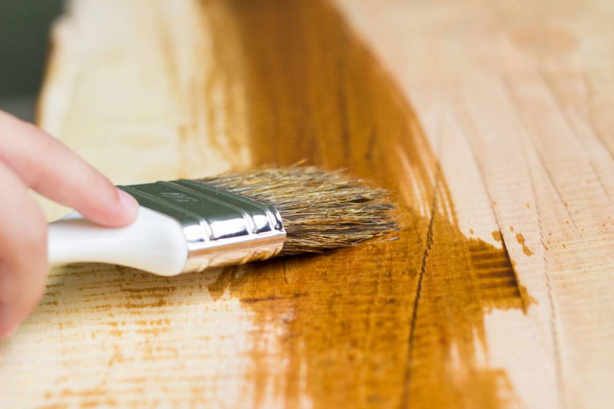  Hand applying varnish to wooden surface with a paintbrush, enhancing wood grain.