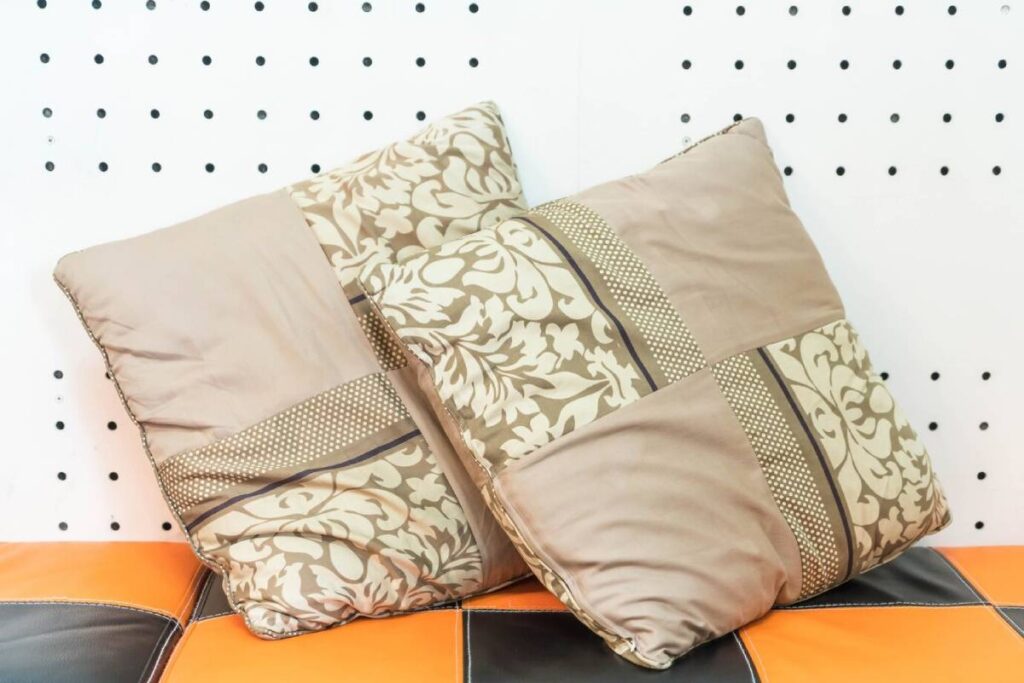 Three decorative pillows with floral and geometric patterns on an orange and black seat against a dotted wall background.