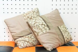 Three decorative pillows with floral and geometric patterns on an orange and black seat against a dotted wall background.