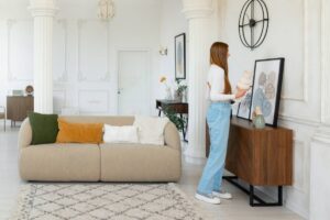Woman arranging vases on a sideboard in a stylish, bright living room with classic white walls and tasteful decor.