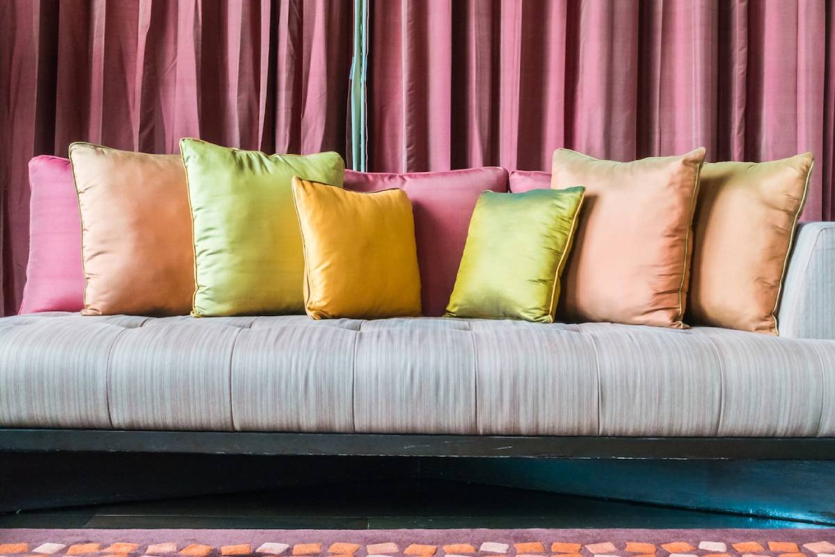  A grey sofa with colourful cushions against a draped pink curtain background.