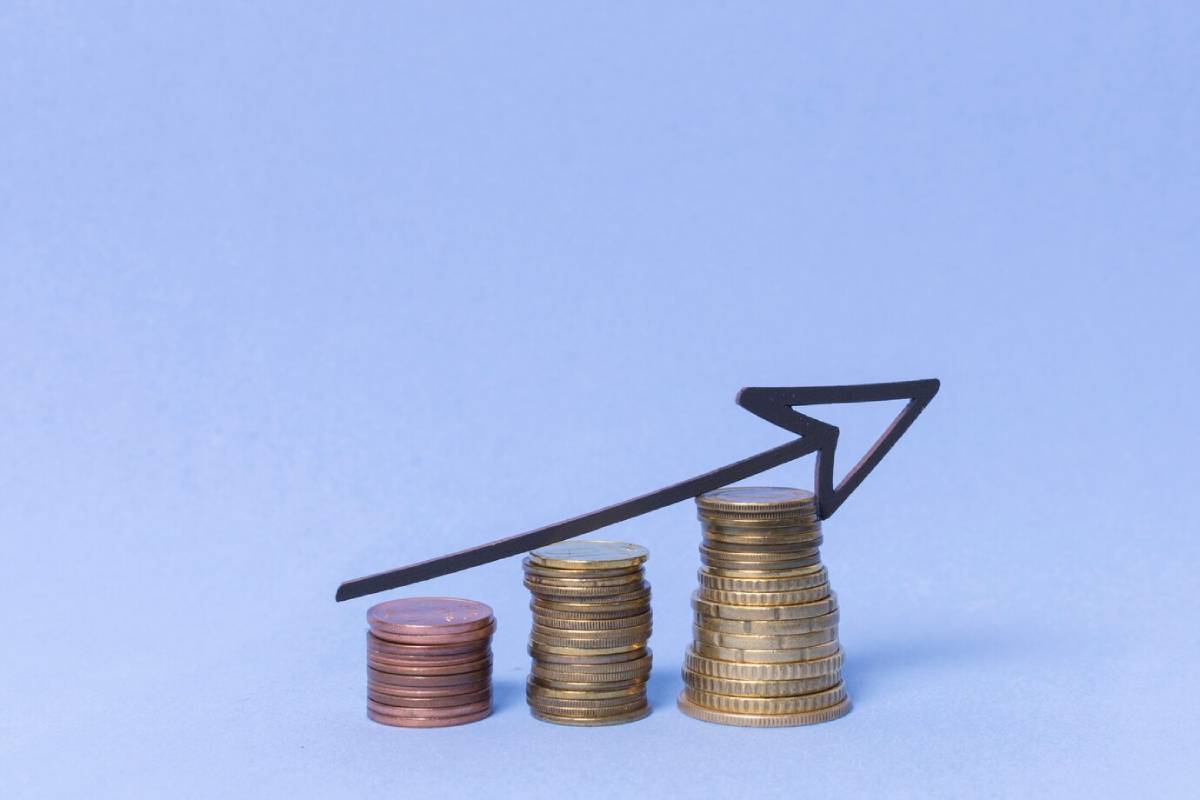 Stacked coins with a rising arrow graph against a blue background, symbolizing financial growth.