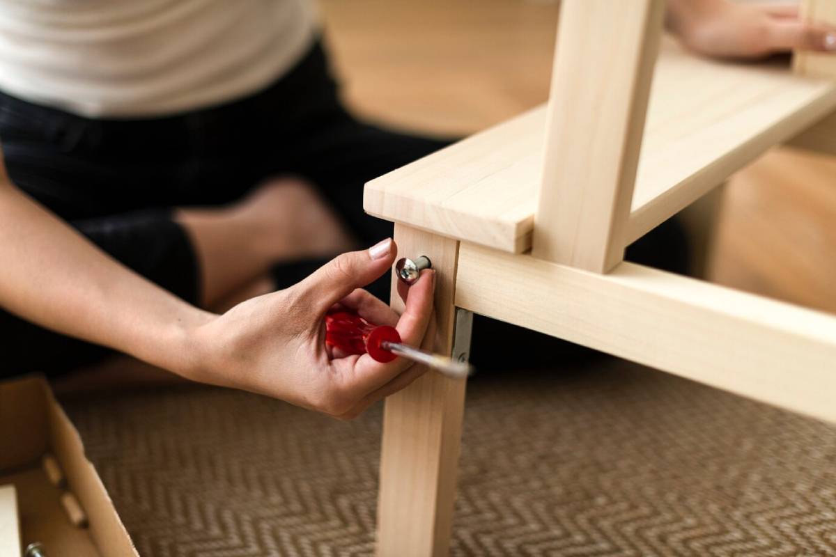 Person assembling furniture, using a screwdriver on wooden parts. 