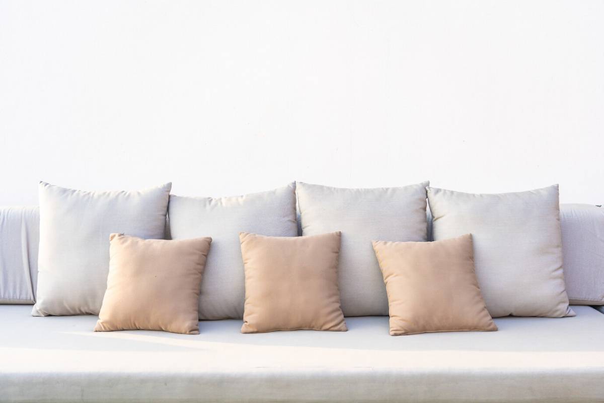  Assorted beige and grey pillows on a simple white couch.