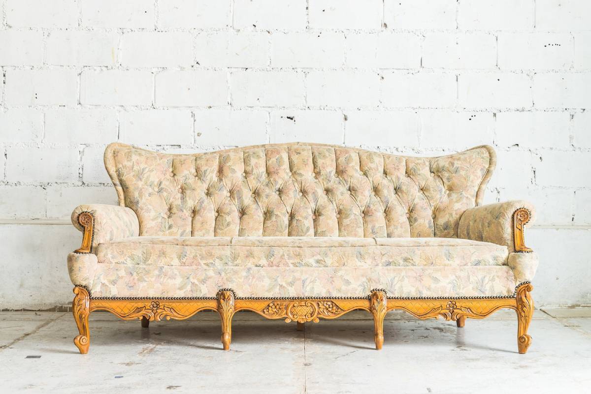 Vintage tufted sofa with floral upholstery against a white brick wall. 