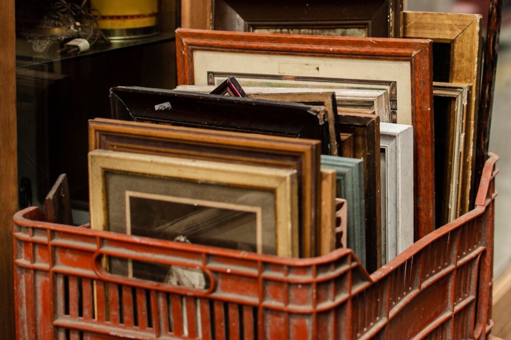 A collection of various old and worn picture frames stacked in an orange wire basket. 