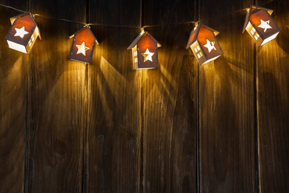 Illuminated star-shaped lanterns hanging against a wooden background, casting warm light and shadows.