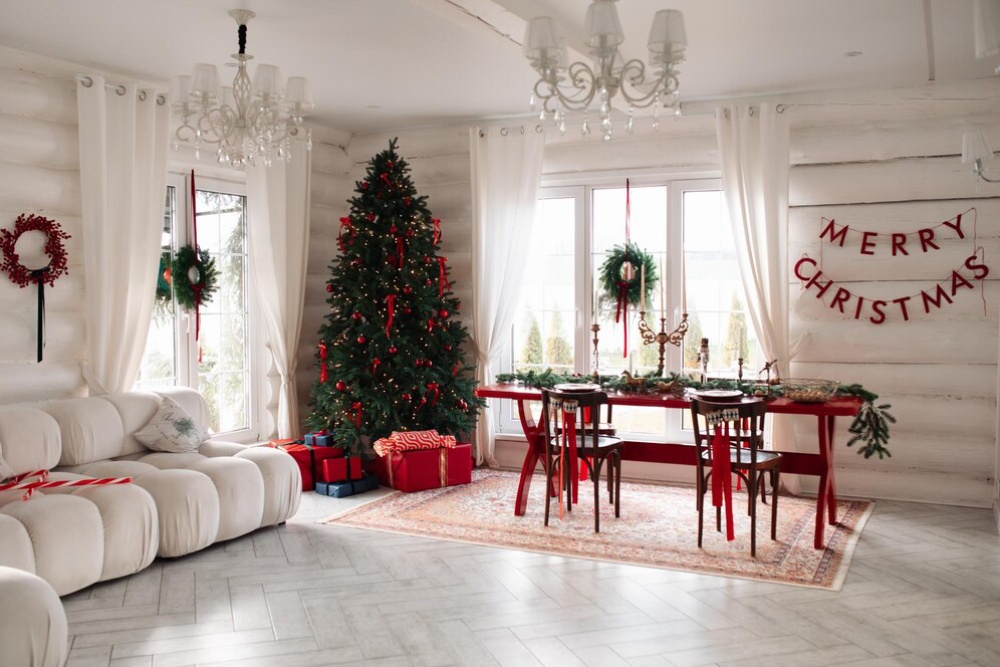 A festive room with a decorated Christmas tree, presents, and a dining table set for Christmas dinner under a "Merry Christmas" banner.