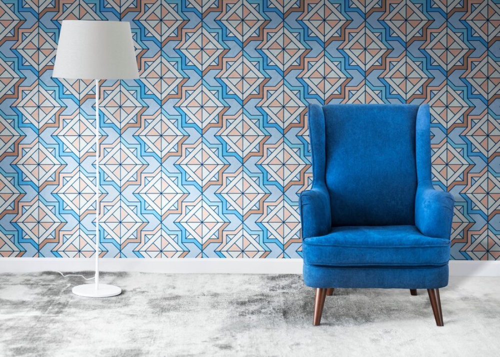 A blue armchair and white floor lamp against a geometric patterned wallpaper in a modern room. 