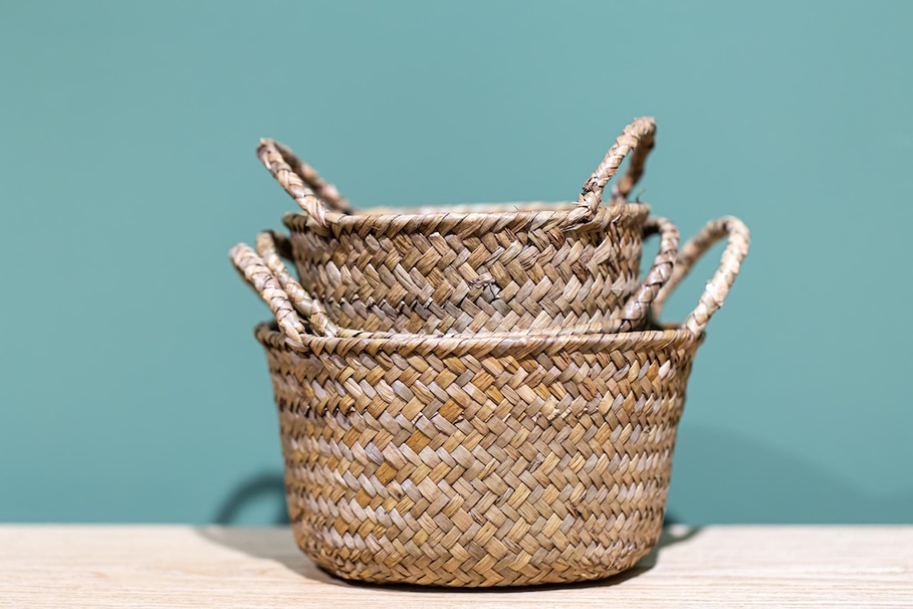   Three nested wicker baskets with handles on a wooden surface against a teal background.