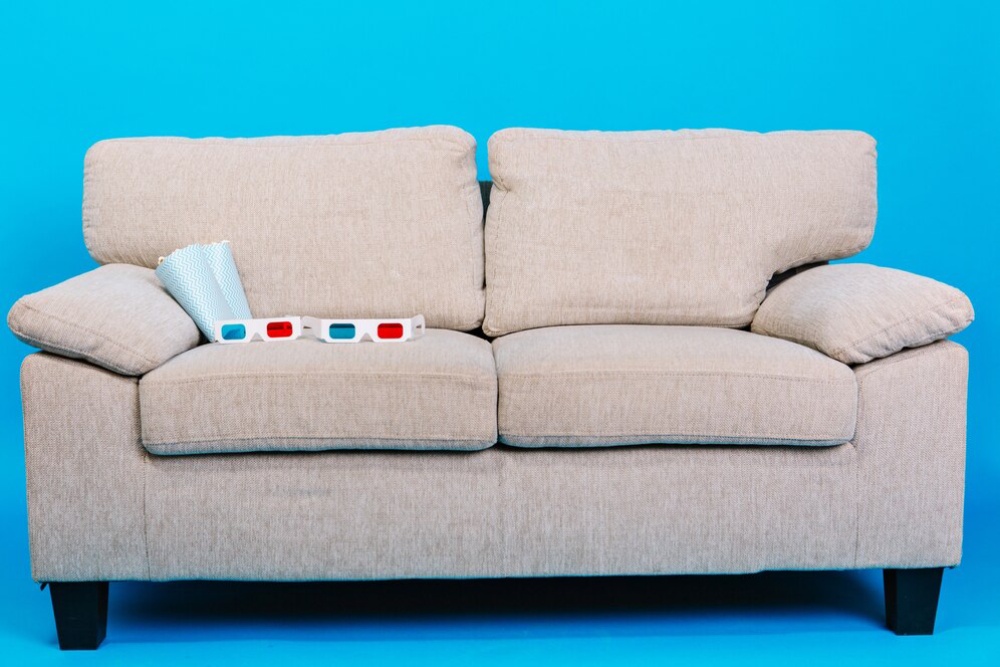   Beige sofa with cushions and 3D glasses on it, set against a bright blue background.