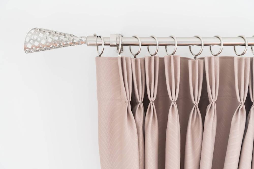  Elegant curtain rod with decorative metal finial and pleated curtains in shades of pink and taupe, against a white background.