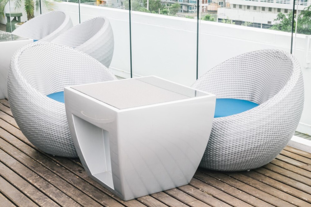  Modern outdoor furniture including two wicker chairs and a square table on a wooden deck, surrounded by a glass barrier. 
