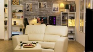 A cosy living room setup featuring a beige sofa, gaming stations, white bookshelves, and wooden wall panels.