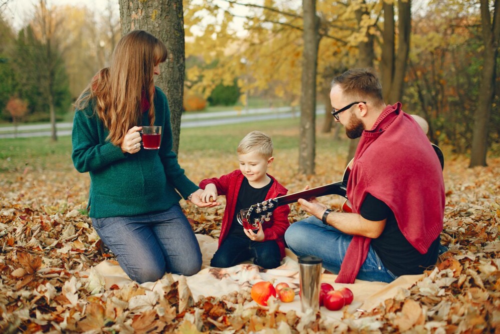  A family enjoys an autumn picnic with music in a leaf-strewn park.