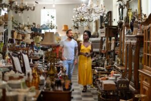 A man and woman browsing an antique shop filled with various items and chandeliers.
