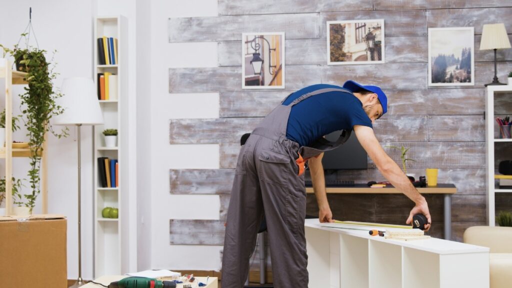 A craftsman measuring a white shelf in a stylishly decorated room.