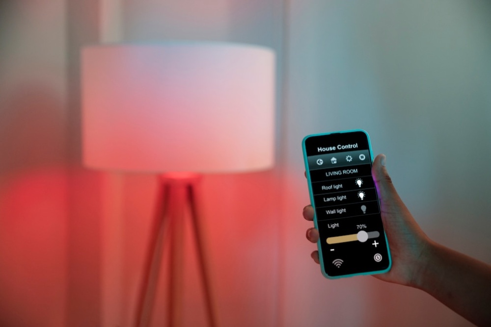 Hand holding a smartphone controlling a lamp colour via an app in a room with ambient lighting. 