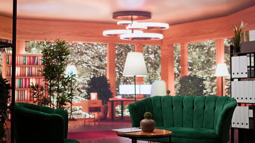  Cozy reading room with green velvet sofa, bookshelves, plants, and modern lighting.