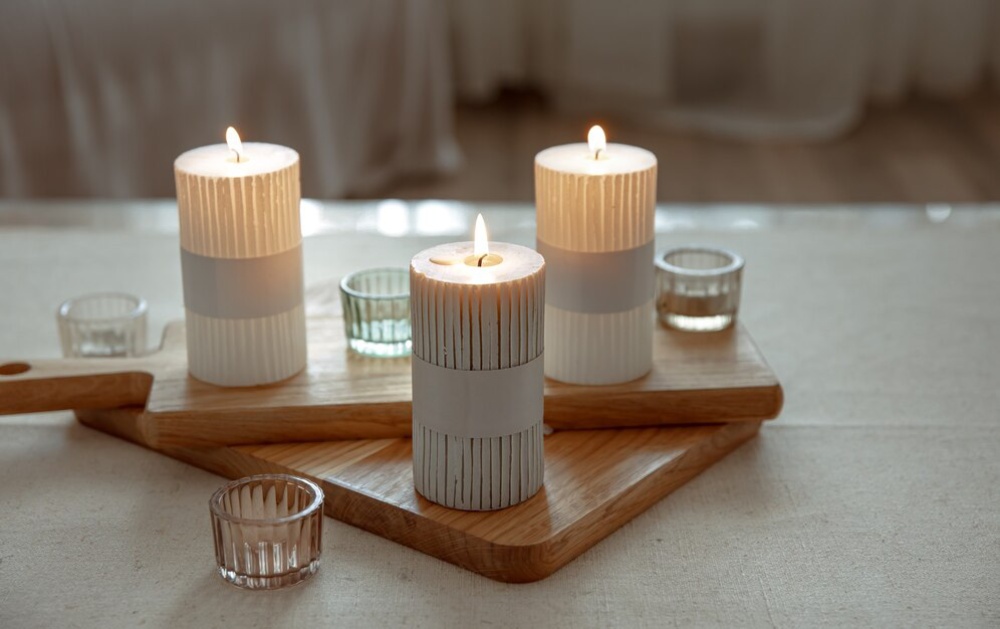 Three lit candles on a wooden tray with glass holders in a softly lit room, creating a tranquil atmosphere. 