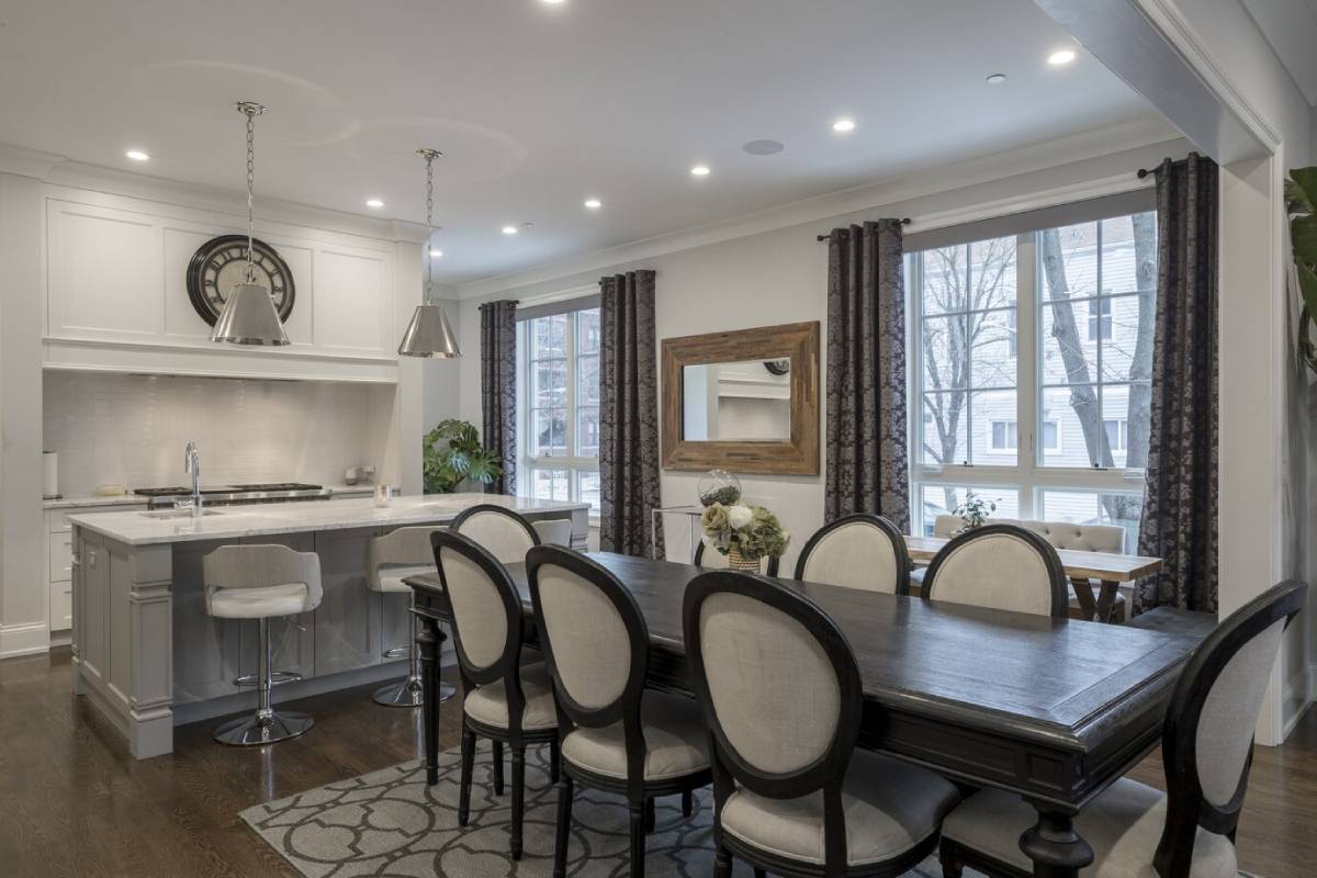 Modern kitchen and dining area with white cabinetry, wooden table, upholstered chairs, and pendant lights, featuring a neutral color palette.