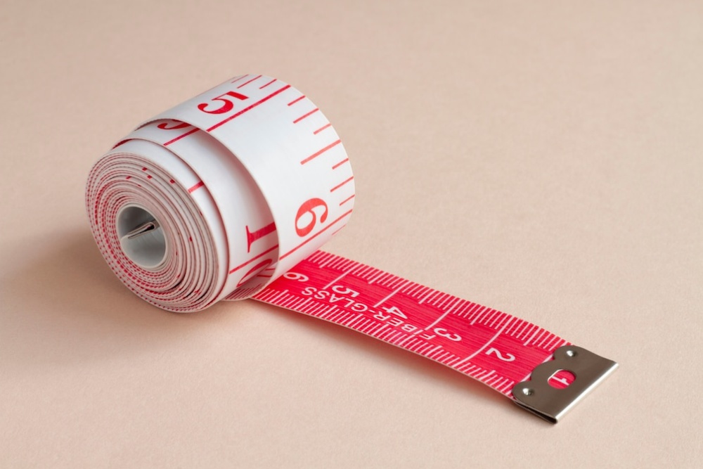   rolled-up white tape measure with red markings on a pale background.