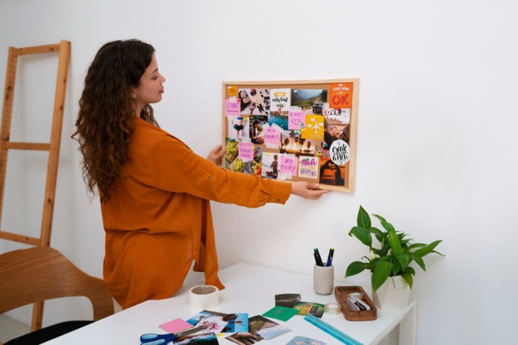 Woman in orange shirt arranges a vision board in a bright office space.