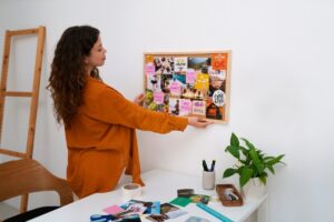 Woman in orange shirt arranges a vision board in a bright office space.