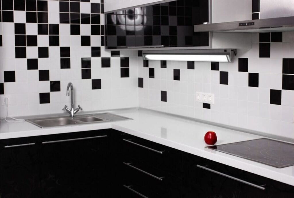 Modern kitchen with black and white tiled backsplash, white countertops, and a solitary red apple.