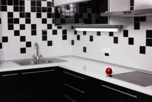 Modern kitchen with black and white tiled backsplash, white countertops, and a solitary red apple.