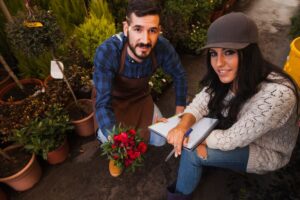 A man and woman discussing plants in a garden centre, surrounded by lush greenery and potted plants.