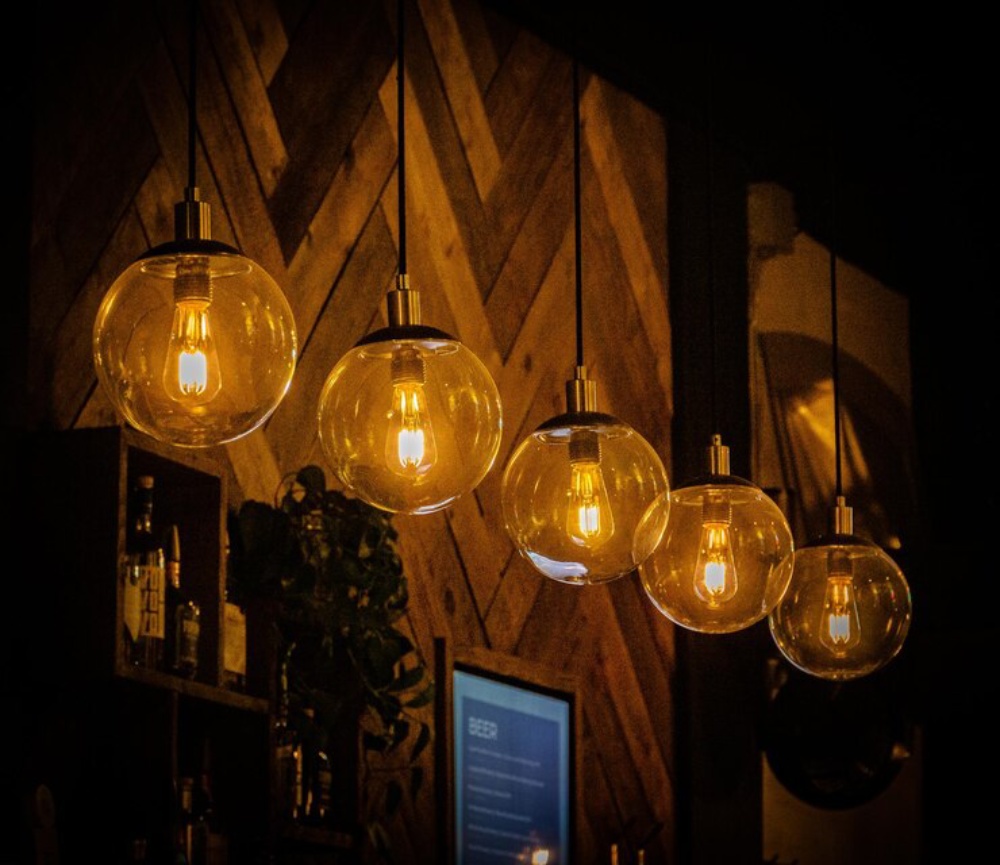 Warm glowing lights hanging from a dark ceiling against a wooden backdrop in a cozy setting. 