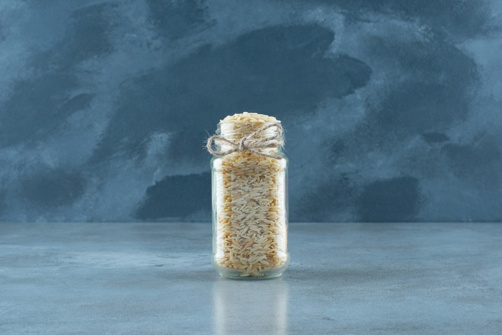 Glass jar filled with rice on a grey textured surface, with a dark grey background.
