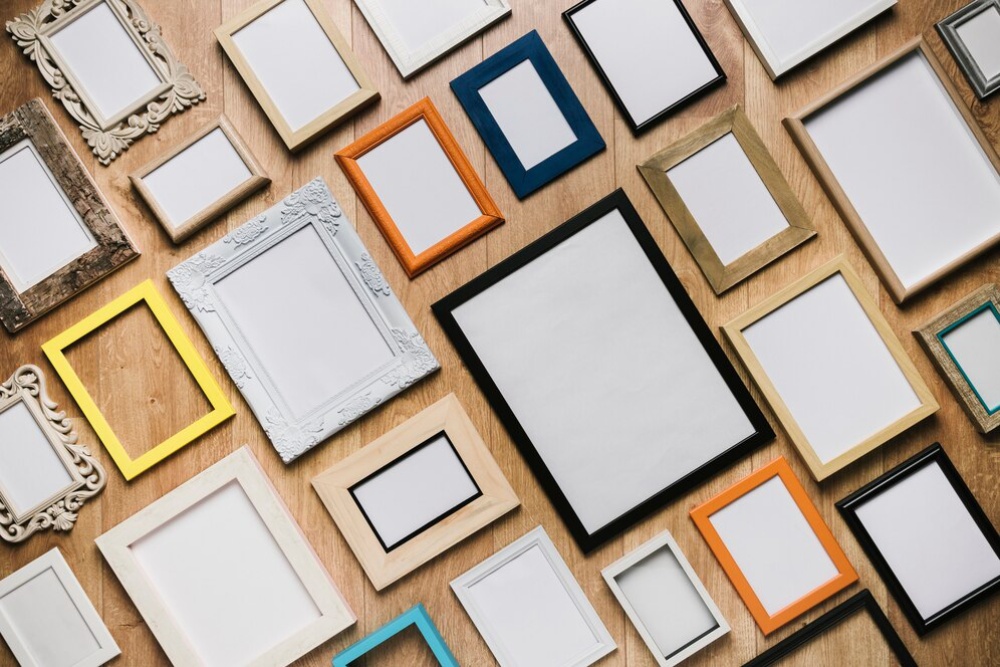  Various empty picture frames of different sizes and colours arranged on a wooden surface.