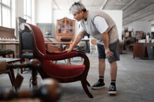 Man in a vintage store examining a classic red upholstered chair.