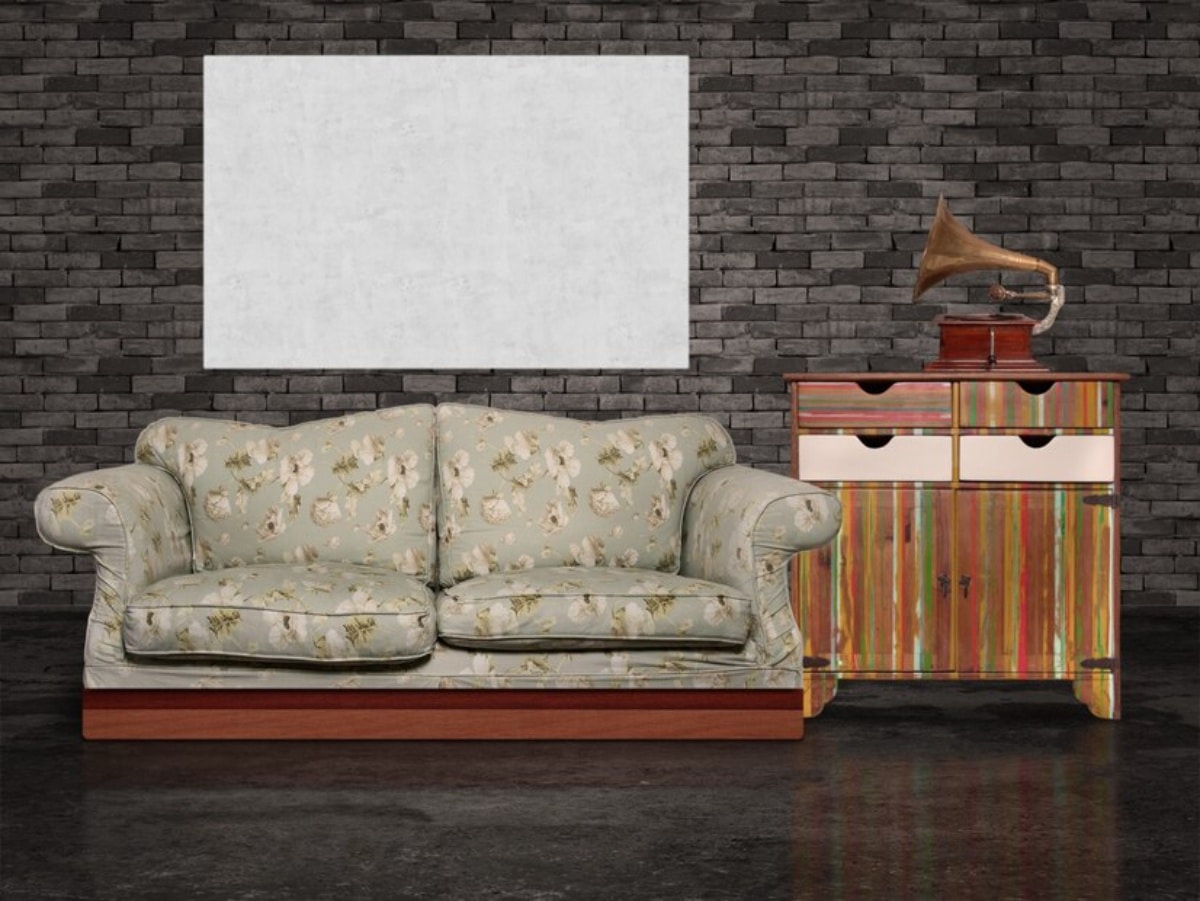 Floral-patterned sofa and colourful striped cabinet with a vintage phonograph against a dark brick wall, empty canvas overhead.