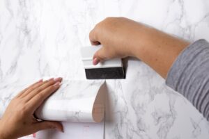 Hands applying a black and white adhesive paper to a surface with a smoothing tool.
