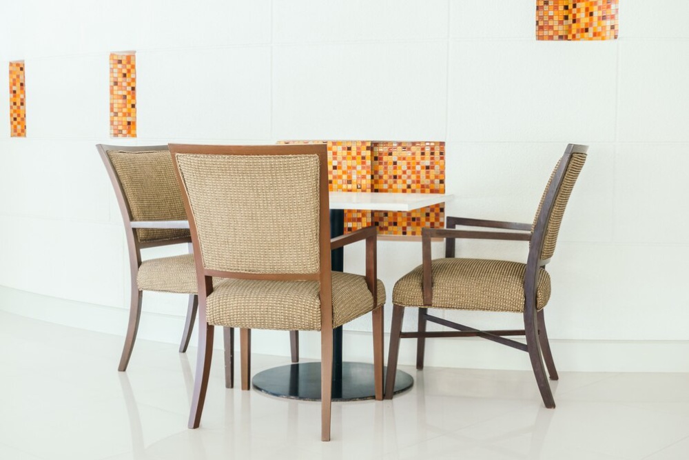  A dining area with a round table and four wicker chairs, against a white wall with decorative mosaic tiles.