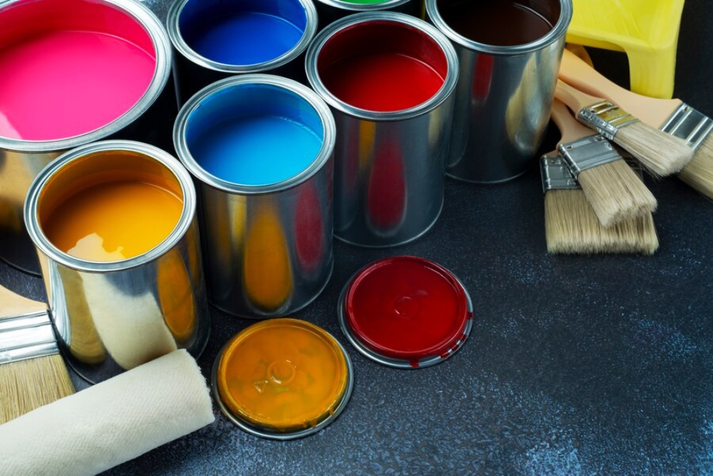  Open paint cans in various colors with brushes on a dark surface.