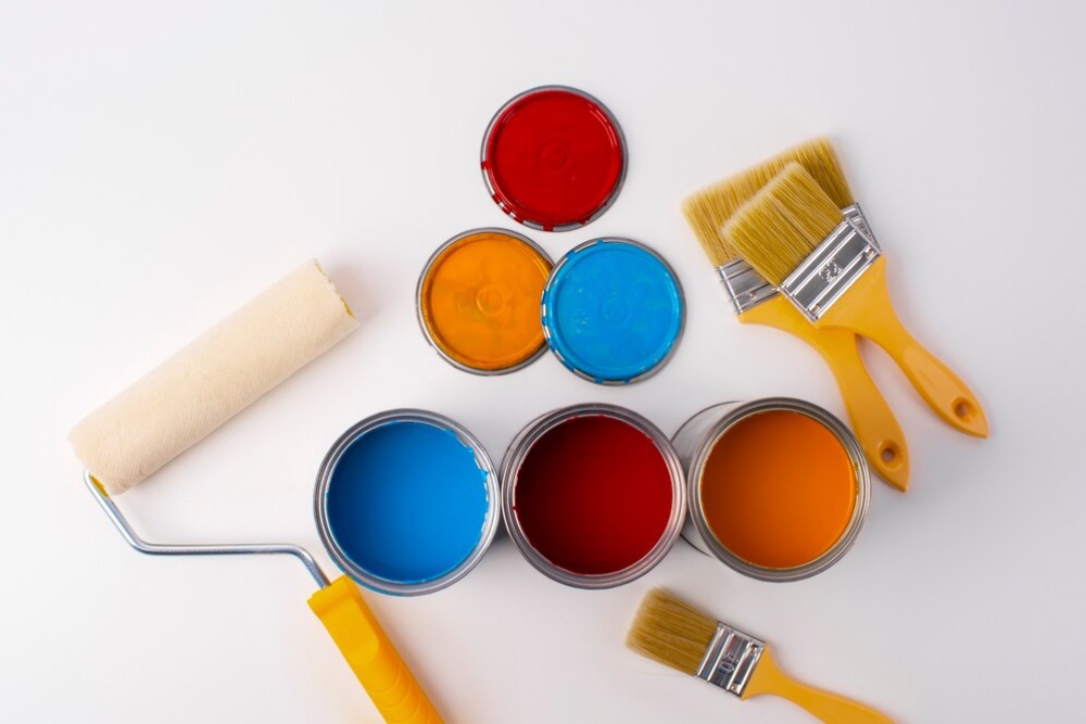 Open paint cans and brushes displaying a range of vibrant red, blue, and orange colors on a white background. 