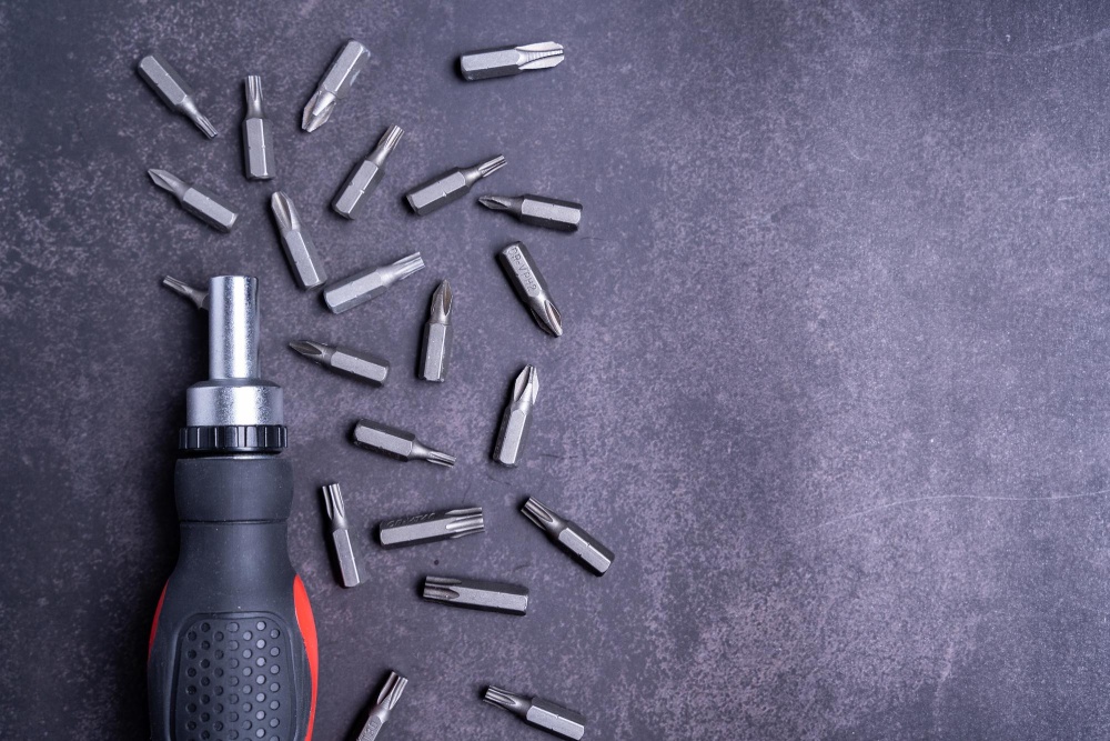  A screwdriver with multiple interchangeable bits scattered on a dark textured surface. 