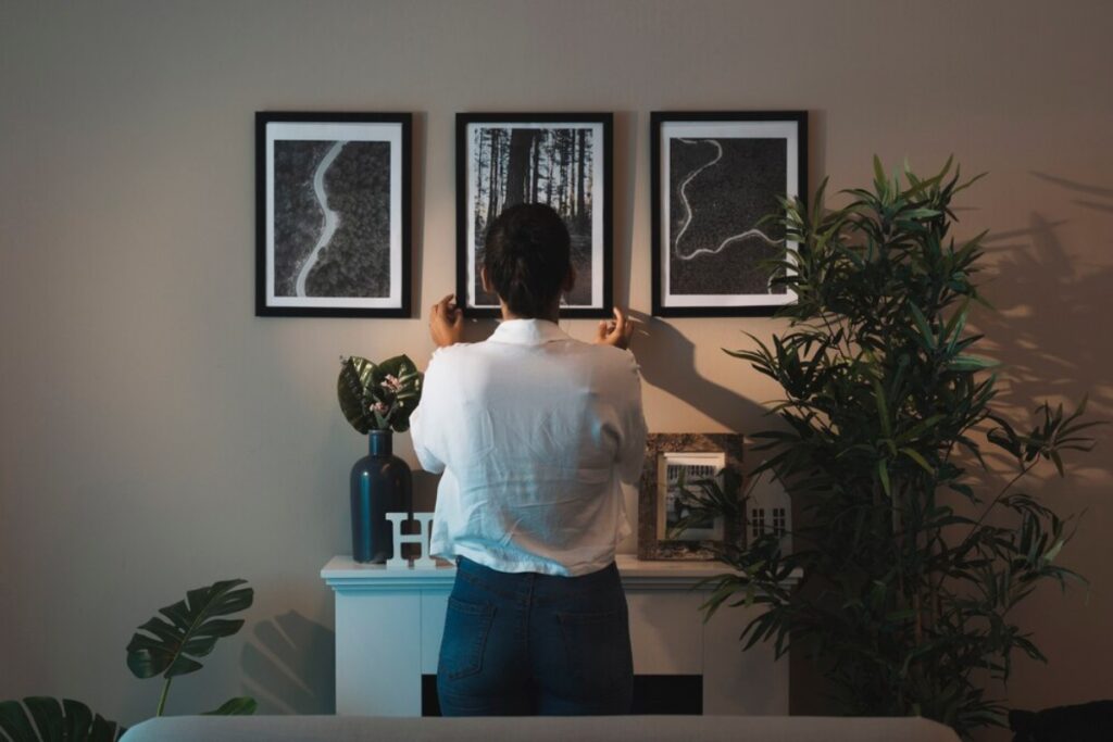 Woman adjusting framed pictures on a wall in a stylishly decorated room.