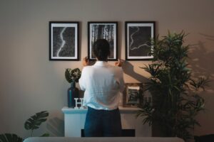 Woman adjusting framed pictures on a wall in a stylishly decorated room.
