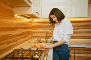 A woman smiling while cutting vegetables in a modern kitchen with wooden accents.