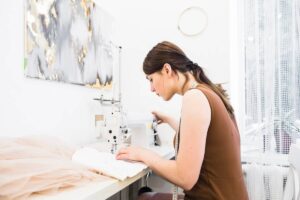 Woman sewing fabric on an industrial sewing machine in a bright workshop with a modern painting on the wall.